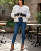 Frau trägt einen kurz geschnittenen weißen Webpelzmantel, blaue Jeans und braune Stiefel im Freien