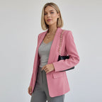 Frau trägt einen rosa Blazer über einem grauen Outfit vor schlichtem Hintergrund.